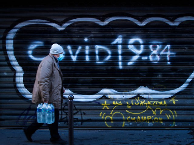 A man wearing a protective mask walks past a boarded restaurant with the writing "Covid 19