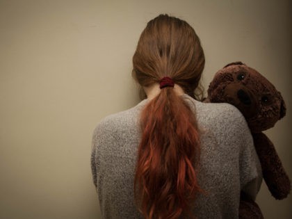 Sad girl with teddy bear standing in the corner.