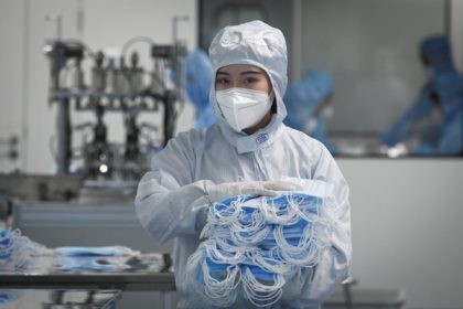 A worker wearing a protective suit holds masks to package at Naton Medical Group, a compan