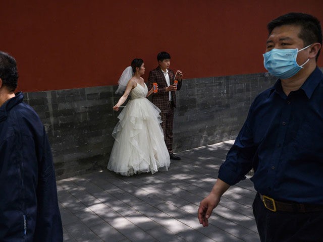 BEIJING, CHINA - APRIL 30: A Chinese woman and man wear protective masks as they take a break to have a drink while taking pictures in advance of their wedding near the Forbidden City, on April 30, 2020 in Beijing, China. Beijing lowered its risk level after more than three …