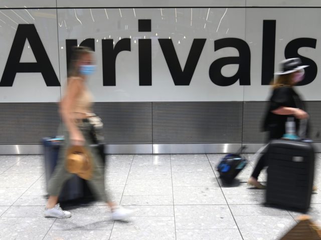 Passengers wearing face masks as a precautionary measure against COVID-19, walk through the arrivals hall after landing at London Heathrow Airport in west London, on January 15, 2021. - International travellers will need to present proof of a negative coronavirus test result in order to be allowed into England, or …