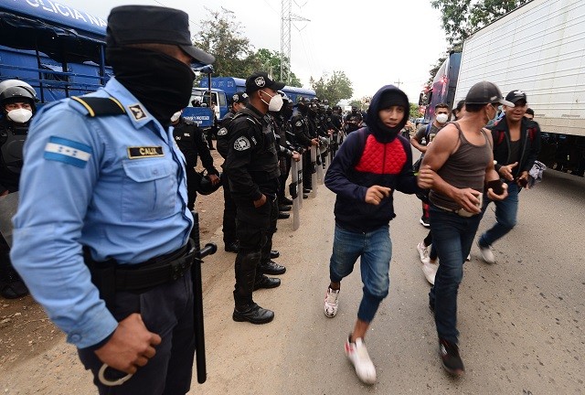 National Police riot police officers observe Honduran migrants moving to Agua Caliente, on the border between Honduras and Guatemala, on their way to the United States, on January 15, 2021. - Hundreds of asylum seekers are forming new migrant caravans in Honduras, planning to walk thousands of kilometers through Central America to the United States via Guatemala and Mexico, in search of a better life under the new administration of President-elect Joe Biden. (Photo by Orlando SIERRA / AFP) (Photo by ORLANDO SIERRA/AFP via Getty Images)