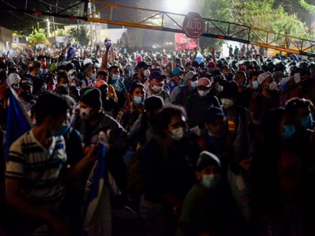 Thousands of Honduran migrants push through the police fence as they attempt to cross the