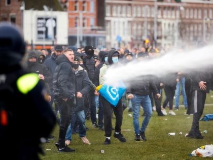 TOPSHOT - Demonstrators are sprayed by police water cannon at Amsterdam's Museumplein during a protest against the lockdown imposed to curb the spread of the Covid-19 pandemic and the outgoing government's policy, on January 21, 2021. (Photo by ROBIN VAN LONKHUIJSEN / ANP / AFP) / Netherlands OUT (Photo by …