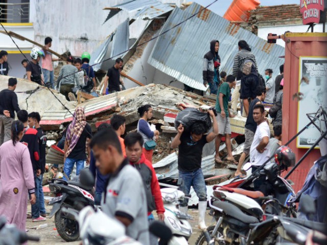 People retrieve goods from a collapsed convenience store as others are seen over building rubble in Mamuju city on January 16, 2021, a day after a 6.2-magnitude earthquake rocked Indonesia's Sulawesi island. (Photo by Firdaus / AFP) (Photo by FIRDAUS/AFP via Getty Images)