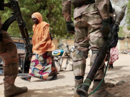 In this photo taken Wednesday, April 8, 2015, a woman walks past Nigerian Soldiers at a ch