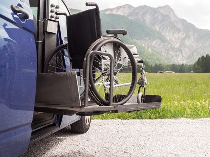Photo of black electric lift specialized vehicle for people with disabilities. Empty wheelchair on a ramp with nature and mountains in the back