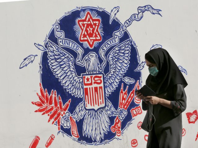 An Iranian woman walks past a mural painted on the outer walls of the former US embassy in