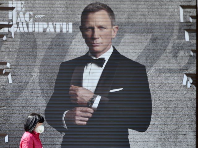 A woman wearing a face mask walks past an image of James Bond actor Daniel Craig in a shop