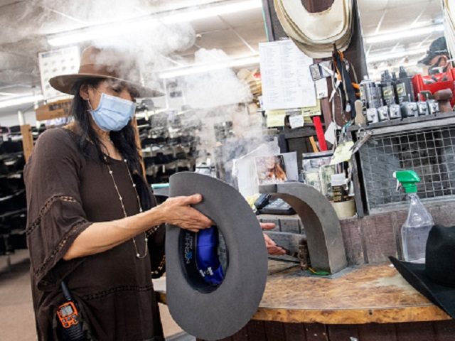A woman shapes a Stetson hat for a client while wearing a mask at the manufacture store on
