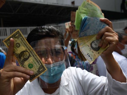 TOPSHOT - A health worker wearing a face mask and shield holds a one dollar bill in one hand and its equivalent in Bolivar bills -his salary- in the other, during a protest for the lack of medicines, medical supplies and poor conditions in hospitals, in Caracas on October 29, …
