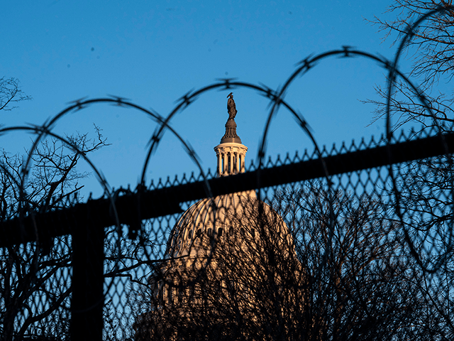 The exterior of the U.S. Capitol building is seen through barbed wire fencing at sunrise o