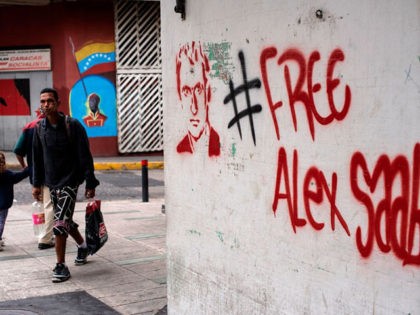 People walk near a graffiti demanding Colombian businessman Alex Saab's freedom, in Caracas, on February 23, 2021. - Saab, who is allegedly close to Venezuelan President Nicolas Maduro and wanted in the US for money laundering, has been put under house arrest in Cape Verde. Saab was detained in June …