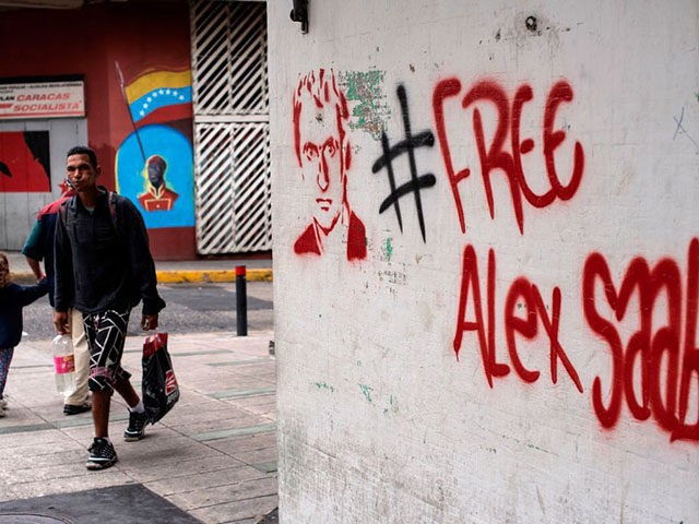 People walk near a graffiti demanding Colombian businessman Alex Saab's freedom, in Caraca