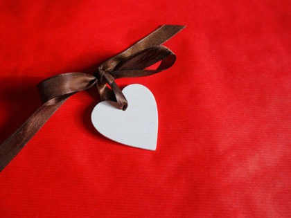 White wooden heart with brown silk bow on red background. Copy space. Love concept. St. Valentine's card