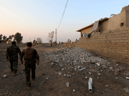 Peshmerga fighters walk past a damaged house in an Iraqi Kurdish Kakai minority village located near the town of Kalak, east of Mosul, on October 26, 2016, after Iraqi forces recaptured it from Islamic State (IS) group jihadists a few months ago. The Kakai are a secretive religious minority that …