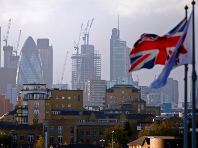 A Union flag flies from a pole as construction cranes stand near skyscrapers in the City o