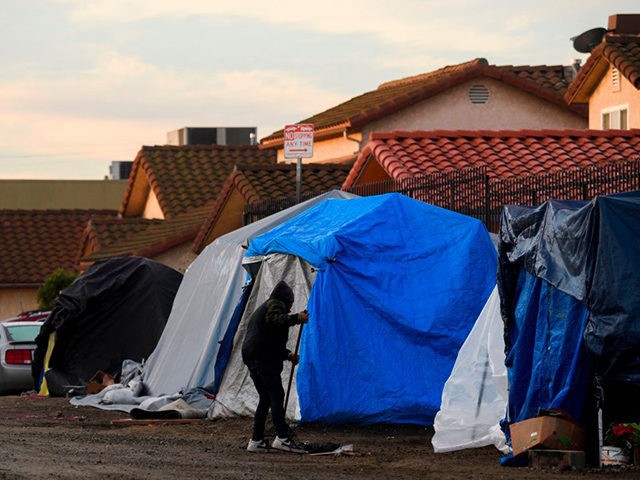 People experiencing homelessness clean the area around their tent shelters before a Los An