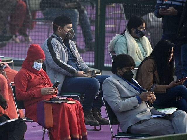 Spectators wearing facemasks use their mobile phones as they wait for the start of the Rep