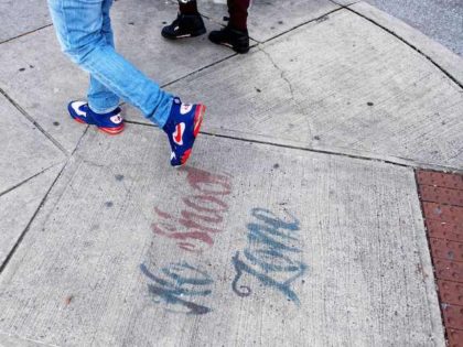 In this file photo, two men walk past a sign spray painted on the sidewalk stating "No Shoot Zone" in Baltimore, MD, on December 17, 2018. (Jim Watson/AFP via Getty Images)