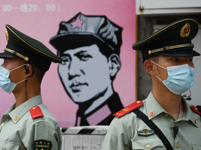 Paramilitary police officers stand guard in front of a poster of late communist leader Mao