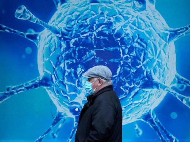 OLDHAM, UNITED KINGDOM - NOVEMBER 24: A man wearing a protective face mask walks past an illustration of a virus outside Oldham Regional Science Centre on November 24, 2020 in Oldham, United Kingdom. England is continuing its second national coronavirus lockdown. People are still permitted to exercise with one other …