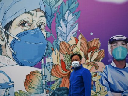 TOPSHOT - A man wearing a face mask walks in front of a mural at the Leishenshan Hospital that had offered beds for coronavirus patients in Wuhan, in Chinas central Hubei province on April 11, 2020. (Photo by Noel Celis / AFP) (Photo by NOEL CELIS/AFP via Getty Images)