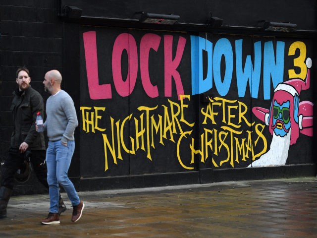 Pedestrians walk past graffiti reading "Lockdown 3: The Nightmare after Christmas" painted on a boarded up restaurant passes a Government Covid-19 information poster near a road in Manchester, northern England, on February 15, 2021. - Britain intends to seek a "cautious but irreversible" ending of strict coronavirus restrictions, Prime Minister …