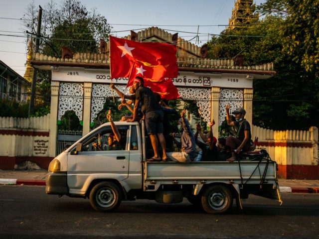 YANGON, MYANMAR - FEBRUARY 09: Protesters waving red flags make three-finger salutes while riding on the back of a pickup truck on February 09, 2021 in Yangon, Myanmar. Myanmar declared martial law in parts of the country, including its two largest cities, as massive protests continued to draw people to …