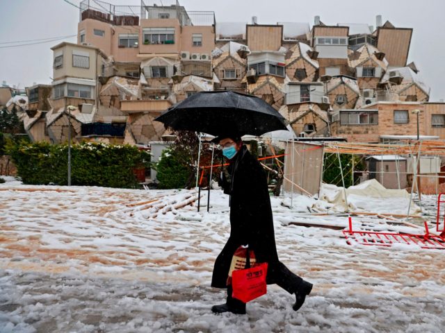 An Ultra-Orthodox Jewish man holds an umbrella as walks on a snow-covered street following