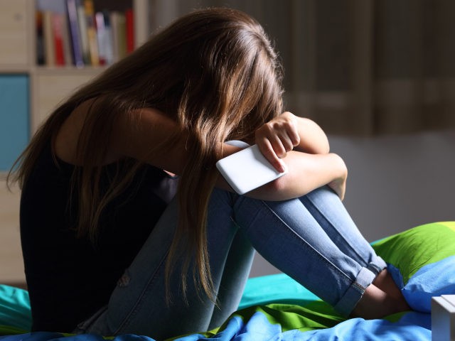 Sad teen with a phone in her bedroom - stock photo Single sad teen holding a mobile phone
