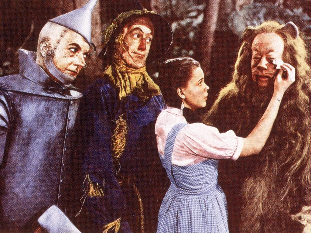 A lobby card from the film 'The Wizard Of Oz,' shows a film still of a scene in which American actress Judy Garland (1922 - 1969) (as Dorothy) wipes tears from the eyes of actor Bert Lahr (1895 - 1967) (as the Cowardly Lion), while watched by Jack Haley (1898 - 1979) (as the Tin Man) (left), and Ray Bolger (1904 - 1987) (as the Scarecrow), 1939. The film was directed by Victor Fleming. (Photo by Hulton Archive/Getty Images)