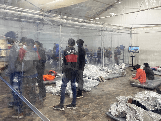 Unaccompanied minors gathered in a crowded room with walls of plastic sheeting at the US C