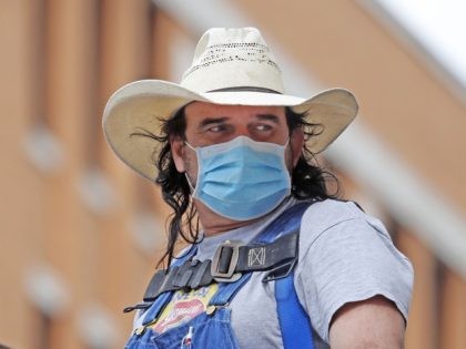 An unidentified man wears a mask and cowboy hat amid concerns of COVID-19 spreading as he