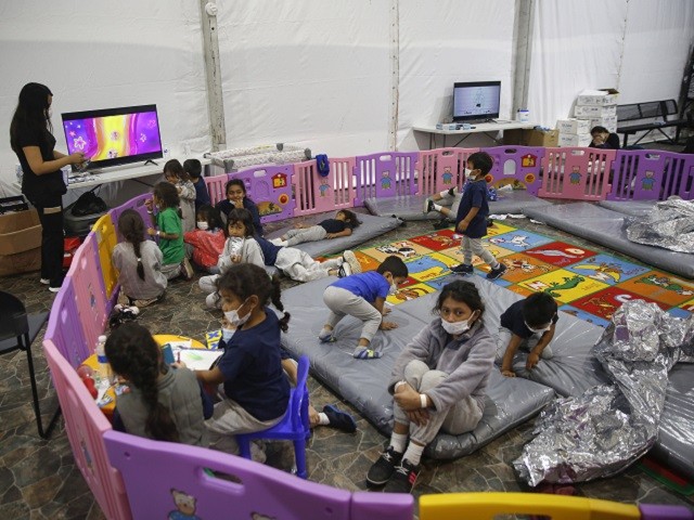 Monitored by a caretaker, young unaccompanied migrants, aged from 3 to 9, watch television inside a playpen at the U.S. Customs and Border Protection facility, the main detention center for unaccompanied children in the Rio Grande Valley, in Donna, Texas, Tuesday, March 30, 2021. The youngest of the unaccompanied minors are kept separate from the rest of the detainees. (AP Photo/Dario Lopez-Mills, Pool)