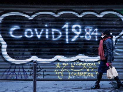 TOPSHOT - A woman, wearing a face mask, walks past the closed iron curtain of a restaurant on which it is written "Covid 19-84" referring to the book of Orwell 1984 on December 10, 2020, as France is on a second lockdown in a biid to contain the spread of …