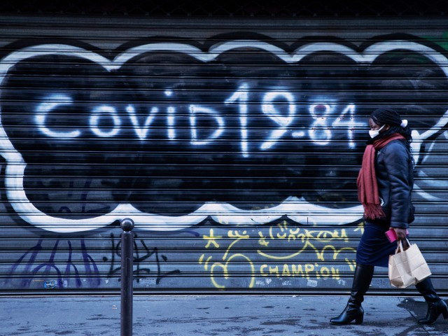 TOPSHOT - A woman, wearing a face mask, walks past the closed iron curtain of a restaurant on which it is written "Covid 19-84" referring to the book of Orwell 1984 on December 10, 2020, as France is on a second lockdown in a biid to contain the spread of Covid-19 pandemic caused by the novel coronavirus. .. . (Photo by JOEL SAGET / AFP) (Photo by JOEL SAGET/AFP via Getty Images)