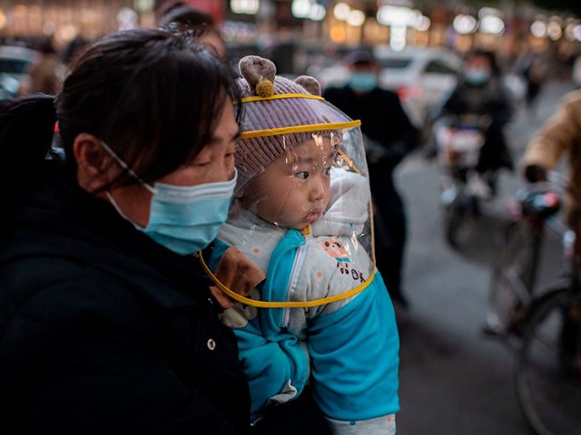 TOPSHOT - A woman wearing a face mask holds a baby that wears a protective shield during rush hour on a street outside of a shopping mall complex in Wuhan on January 13, 2021. - A team of WHO experts will land directly in Wuhan on January 14, 2021, China's foreign ministry said, starting their long-delayed probe into Covid-19 at the virus epicentre. (Photo by NICOLAS ASFOURI / AFP) (Photo by NICOLAS ASFOURI/AFP via Getty Images)
