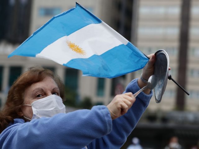 A woman bangs the lid of a pot while carrying the Argentine national flag during a demonstration called by small businessmen affected by the government's mandatory quarantine imposed for more than 13 weeks, protesting the quarantine and the expropriation of the Vicentin agro-industrial company on the Obelisk in Buenos Aires, …