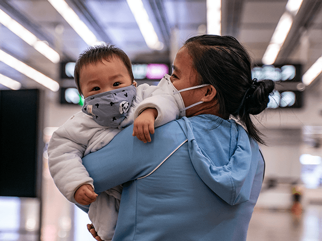 A woman carries a baby wearing a protective mask as they exit the arrival hall at Hong Kon