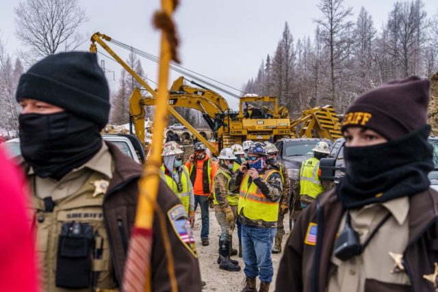 Construction workers stand behind Aitkin County sheriff officers as environmental activist protest at the construction site for the Line 3 oil pipeline site near Palisade, Minnesota on January 9, 2021. - Line 3 is an oil sands pipeline which runs from Hardisty, Alberta, Canada to Superior, Wisconsin in the United …