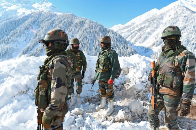 Indian army soldiers stand on a snow-covered road near Zojila mountain pass that connects