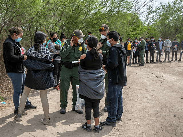 U.S. Border Patrol agents question families as a group of unaccompanied minors (R), awaits Border Patrol transport after they crossed the-Rio Grande into Texas on March 25, 2021 in Hidalgo, Texas. A large group of families and unaccompanied minors, mostly teenagers, came across the border onto private property, where Border …