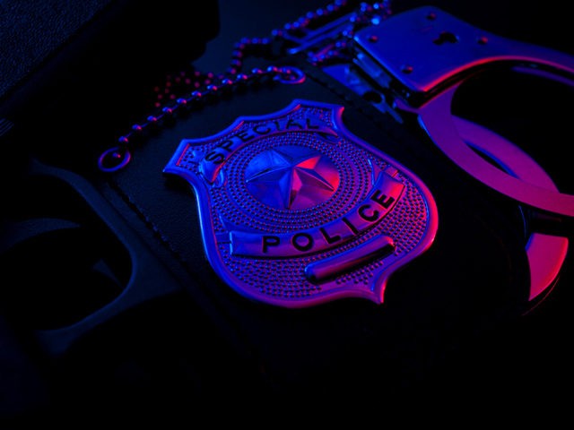 Police raid at night and you are under arrest concept with a police badge, gun and a pair of handcuffs at night illuminated by the flashing red and blue police lights
