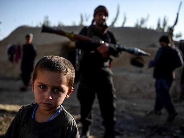IIn this photo taken on September 27, 2020, a young boy looks at the camera as a policeman holding a rocket-propelled grenade (RPG) stands behind in a house at Deh Qubad village in Maiwand district of Kandahar province. - The dry and dusty village of Aziz Abad in Maiwand district …