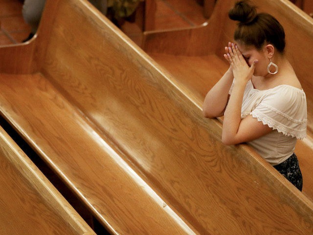 A woman bows her head in St Pius X Church at a vigil for victims after a mass shooting whi