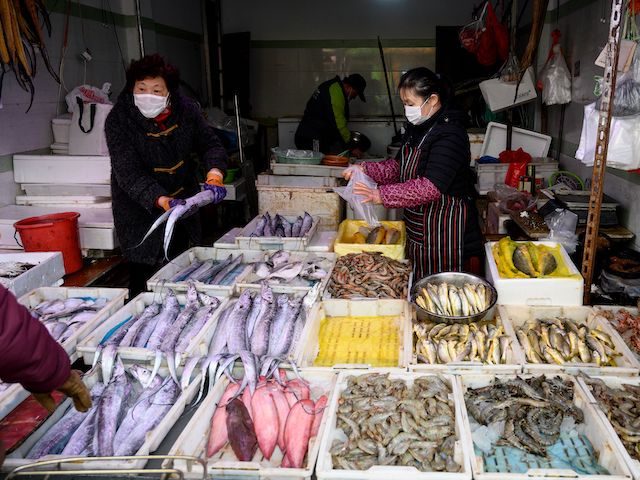 A seafood vendor (R) wearing a face mask talks to a customer at a wet market in Shanghai o