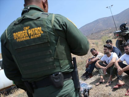SAN DIEGO, CA - JULY 16: A U.S. Border Patrol agent monitors a group of apprehended males from India who illegally crossed the U.S.-Mexico border on July 16, 2018 in San Diego, California. The entire Southwest border saw 34,114 U.S. Border Patrol apprehensions in the month of June compared with …