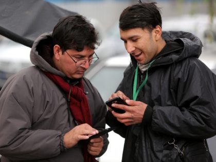 A bike-delivery food messenger stands next to another man as they both use smartphones alo