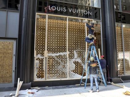 Workers begin to board up a display window at the Louis Vuitton store Monday, Aug. 10, 202